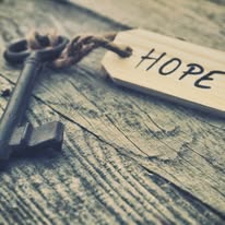 Key with "Hope" tag on wood surface.